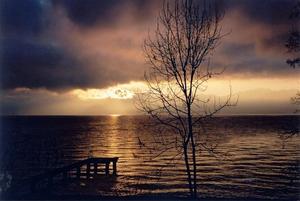 Sun setting over lake, dark cloud, trees, pier and alps